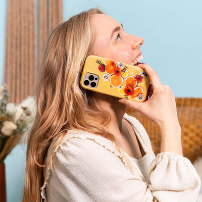 A smiling woman looks up while holding an iPhone with a Presidio Edition: Pucker Up Posie Collection case on it