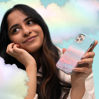 A young woman surrounded by clouds smiles while holding an iPhone with a Presidio Edition: Dreams Come True Collection case on it
