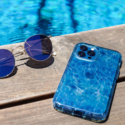 An iPhone with a Presidio Edition: Summer Essentials Kit case on it sits face down next to a pair of sunglasses by the pool