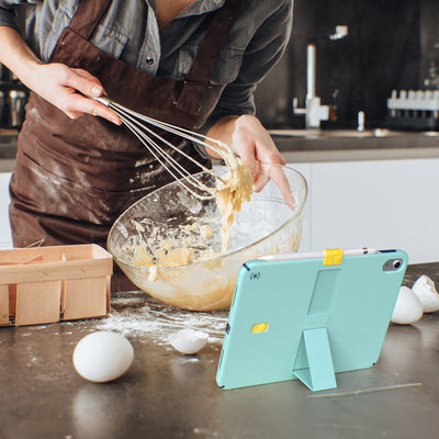 Image of a woman cooking in a messy kitchen with a StandyShell in view stand formation in front of her.#color_glass-teal-deep-sea-blue-daisy-yellow