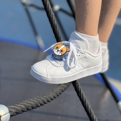 Lifestyle photo of a close-up of a child wearing a shoe on a playground with Tagimal Milo, the orange dog, tied to his laces#color_blaze-milo-mittens-and-tink