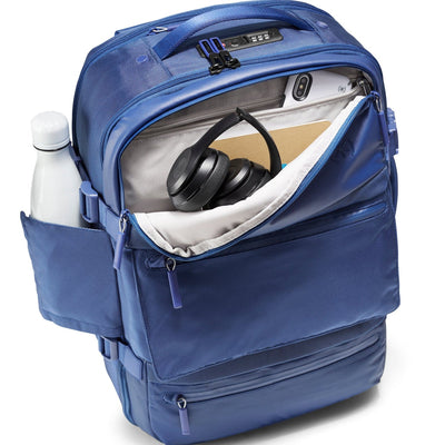 Three-quarter top-down view of Speck Travel Backpack in Macaw Blue with front top pocket revealing contents and water bottle in side pocket.#color_macaw-blue