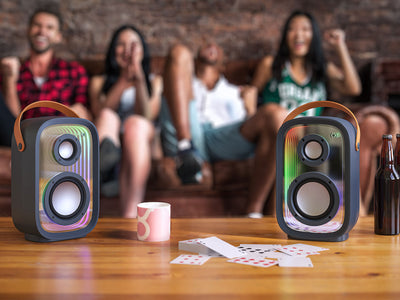 Four people sitting on a couch at a party with multiple Gemtones Infinity speakers on a table in front of them