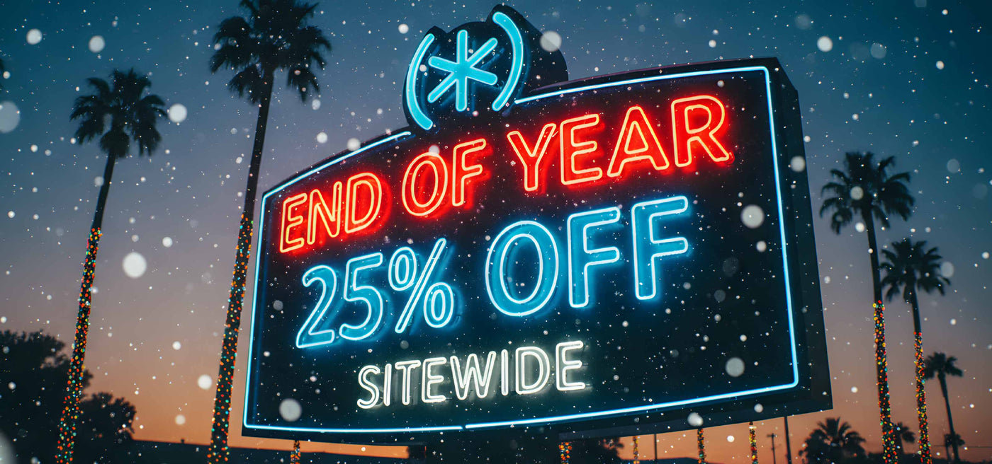 A neon sign lit up at dusk with palm trees lighted with Christmas lights in the background. Sign reads End Of Year 25% OFF Sitewide