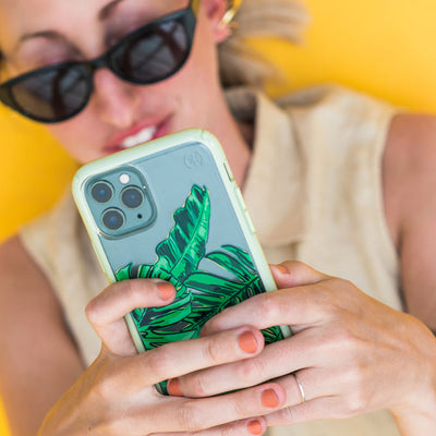 Woman with sunglasses on laying on her back holding iPhone with Presidio Perfect-Clear + Print: Palms Collection case above her