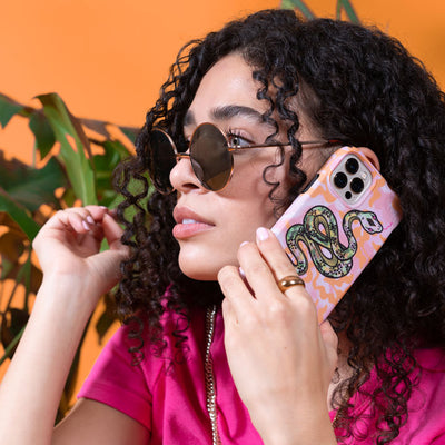 A young woman in sunglasses holding an iPhone to her ear with a Presidio Edition: Sage Serpent Collection case on it