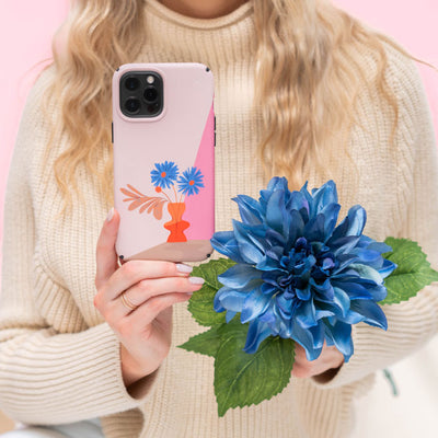 A woman in a sweater holding an iPhone with the Presidio Edition: Blue Bouquet Collection case in one hand and a blue flower in the other