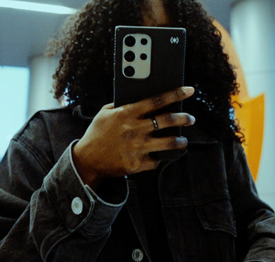 A woman holds a Samsung S24 Ultra phone in a black Speck Presidio2 Grip case
