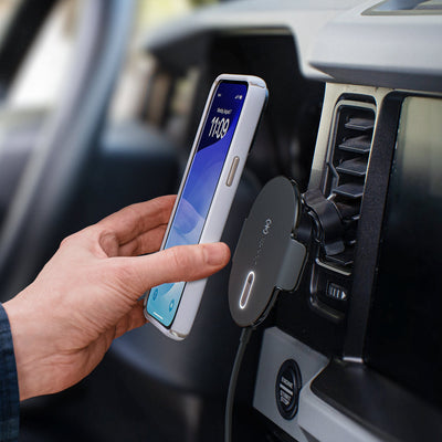 Photo of a hand attaching a smartphone to the magnetic charging car vent mount which is fastened to dashboard vents of a vehicle#color_black