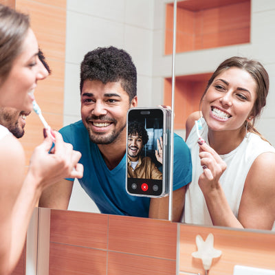 Photo of a couple brushing their teeth while video calling a friend on a smartphone attached to a mirror with Everywhere Mount#color_black-slate-grey