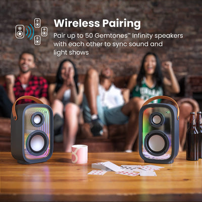 Four people sitting on a couch at a party with multiple Gemtones Infinity speakers on a table in front of them. Wireless pairing - pair up to 50 Gemtones Infinity speakers with each other to sync sound and light shows#color_dark-grey-chrome-tan