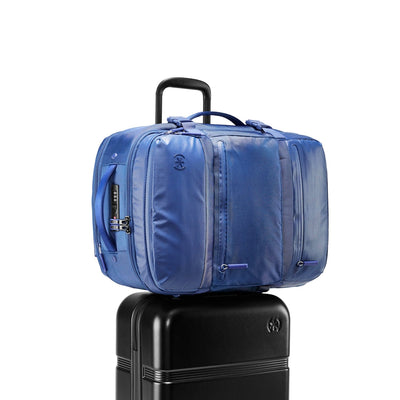 Three-quarter front view of Speck Travel Backpack in Macaw Blue sitting on top rolling luggage with the luggage handle passing through the backpack rear sleeve.#color_macaw-blue