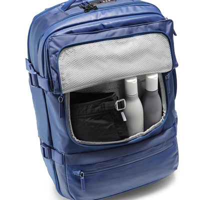 Three-quarter top-down view of Speck Travel Backpack in Macaw Blue with front Wet Pocket open revealing swimsuit and liquid containing bottles inside.#color_macaw-blue