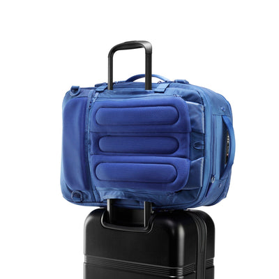 Three-quarter rear view of Speck Travel Backpack in Macaw Blue sitting on top rolling luggage with the luggage handle passing through the backpack rear sleeve.#color_macaw-blue